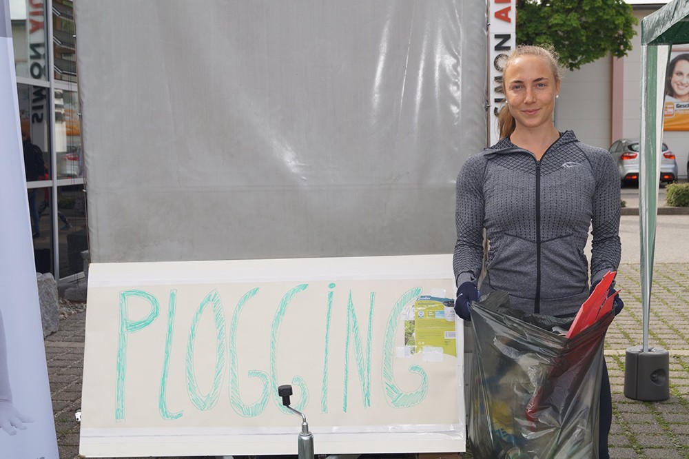 Frau mit Müllsack vor "Plogginglauf"-Schild